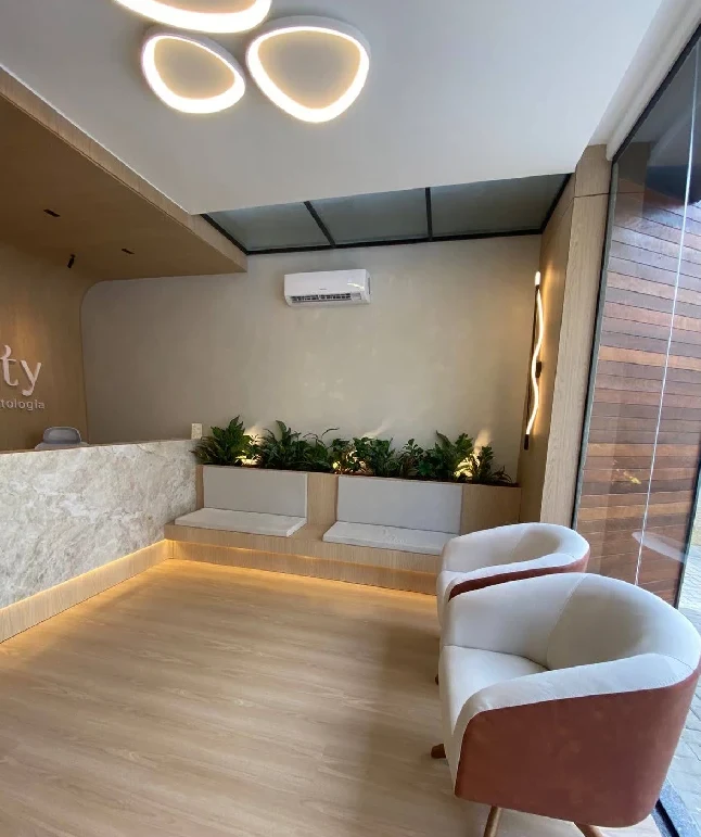 Sala de espera com poltronas claras, banco de madeira e plantas