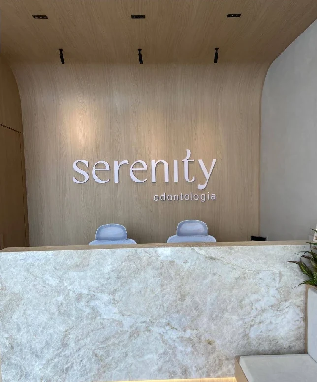Recepção da Serenity: painel de madeira clara em curva, letreiro serenity e balcão de mármore