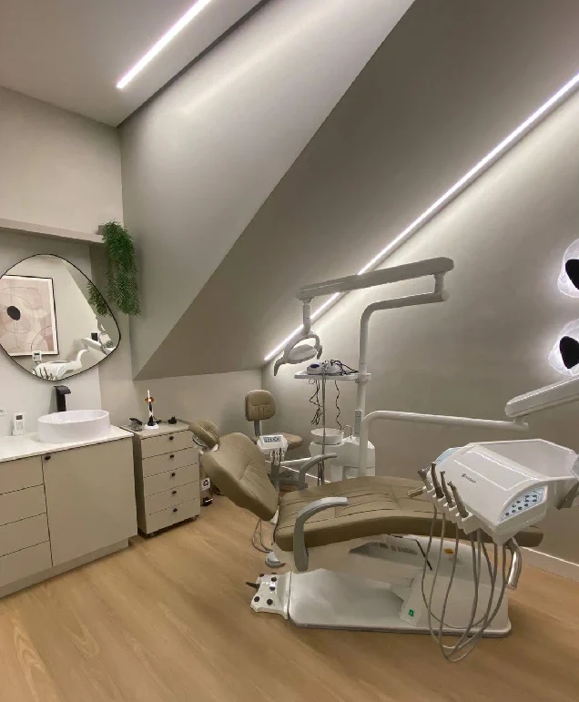 Sala de atendimento com teto inclinado, cadeira odontológica e faixas de luz