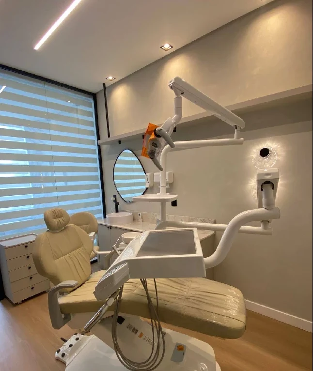 Sala de atendimento com cadeira odontológica, espelho e luz no teto
